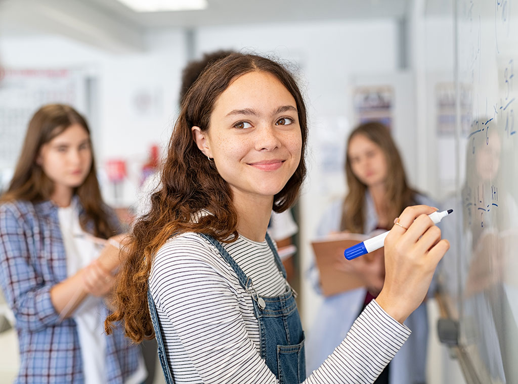 Mädchen schreibt an Tafel und lächelt ins Bild